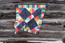 Load image into Gallery viewer, Canadian Diamond quilt pattern by Penny Spool Quilts, featuring four large diamonds surrounded by half-square triangles and a pieced border. Quilt shown in navy with pink, yellow, aqua and white accents, hanging from log wall.