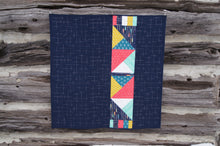 Load image into Gallery viewer, Canadian Diamond quilt pattern by Penny Spool Quilts, featuring four large diamonds surrounded by half-square triangles and a pieced border. Picture shows back of quilt in navy with pink, yellow, aqua and white accents, hanging from log wall.