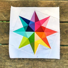 Load image into Gallery viewer, Rainbow Star Quilt Block Pattern by Penny Spool Quilts. Eight pointed star in rainbow solid fabrics on white background, shown on wood floor.