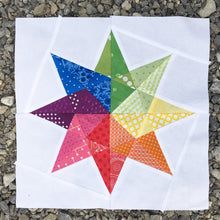 Load image into Gallery viewer, Rainbow Star Quilt Block Pattern by Penny Spool Quilts. Eight pointed star in rainbow print fabrics on white background, on gravel.