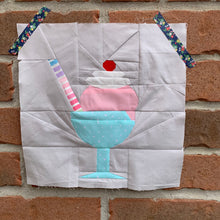 Load image into Gallery viewer, Ice Cream Bowl quilt block pattern by Penny Spool Quilts. Part of the Ice Cream Sunday collection. Sample shows pink ice cream topped with whipped cream and a red cherry, with a striped straw, in a light blue bowl with stem, on white background. Shown on red brick wall