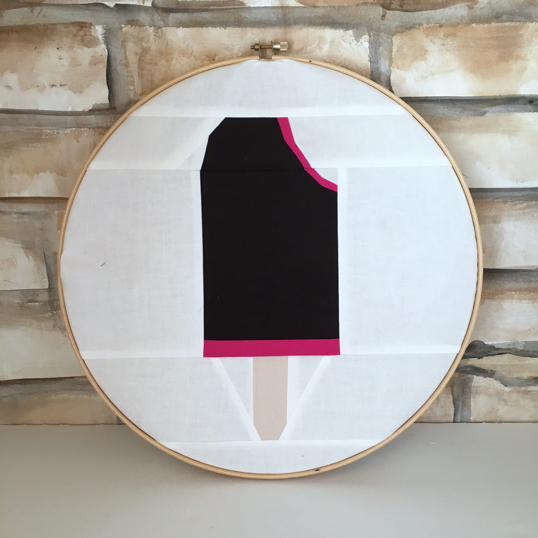 Ice Cream Bar 2 foundation paper pieced quilt block pattern by Penny Spool Quilts. Shows raspberry chocolate ice cream bar with bite out top corner, on white background fabric, framed in embroidery hoop