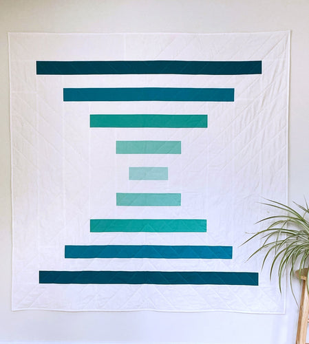 Raise the Bar quilt pattern by Penny Spool Quilts - Sample quilt in turquoise ombre and white on white wall